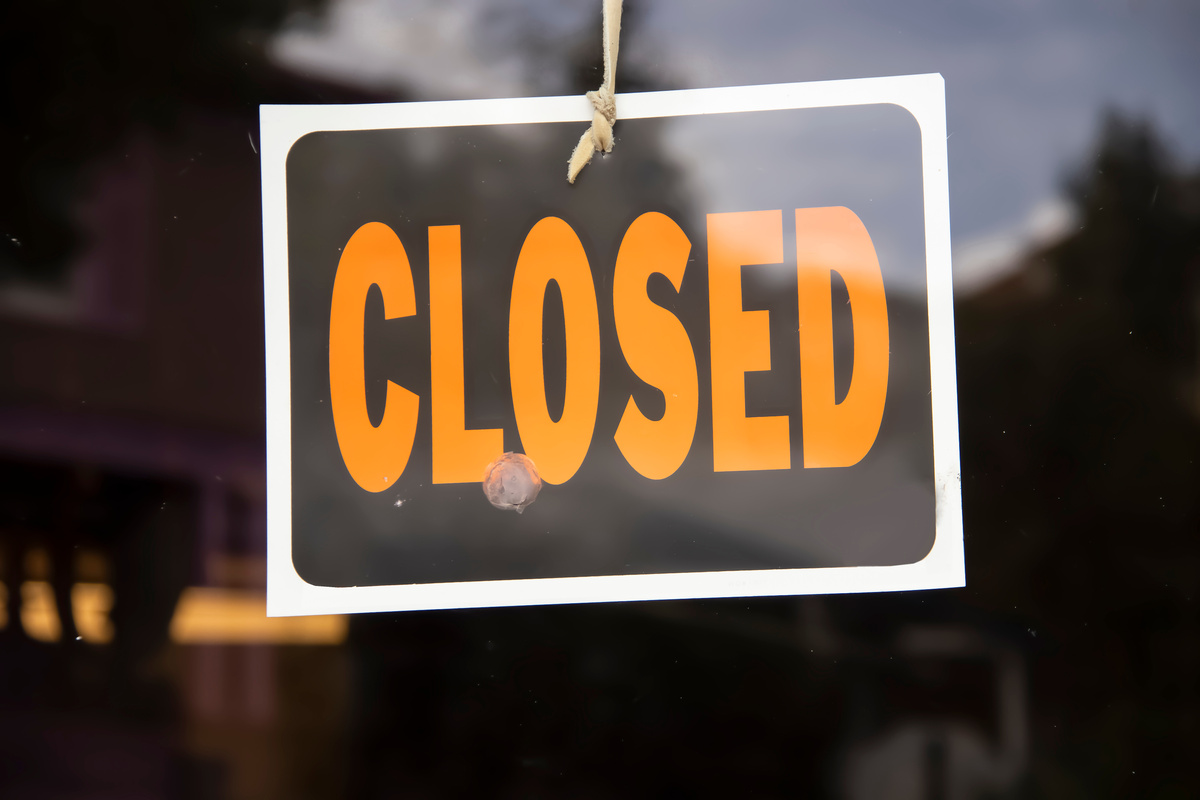 Closed sign hanging in business window by a string - crooked with glob of glue also attaching it to window - some abstract reflections